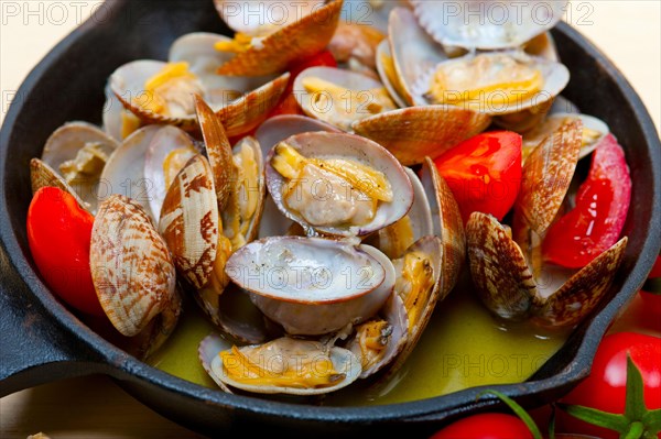 Fresh clams stewed on an iron skillet over wite rustic wood table