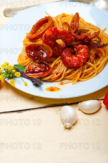 Italian seafood spaghetti pasta on red tomato sauce over white rustic wood table