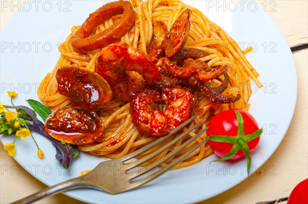 Italian seafood spaghetti pasta on red tomato sauce over white rustic wood table