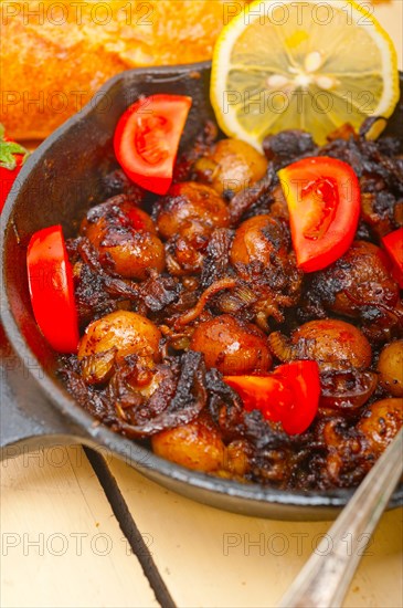 Baby cuttle fish roasted on iron skillet with tomatoes and onions over rustic wood table