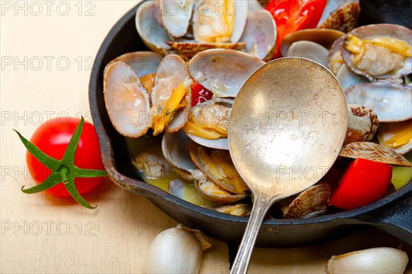 Fresh clams stewed on an iron skillet over wite rustic wood table