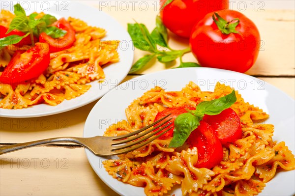 Italian pasta farfalle butterfly bow-tie with tomato basil sauce over white rustic wood table