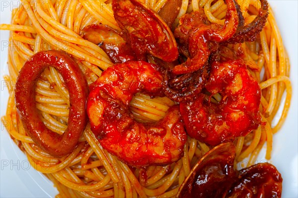 Italian seafood spaghetti pasta on red tomato sauce over white rustic wood table