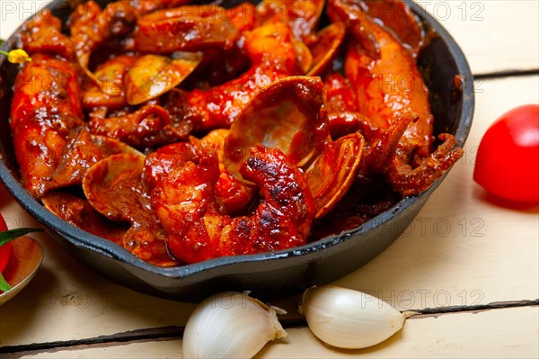 Fresh seafood stew prepared on an iron skillet ove white rustic wood table