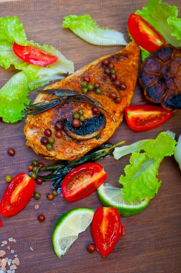 Wood fired hoven cooked chicken breast on wood board with herbs spices and vegetables