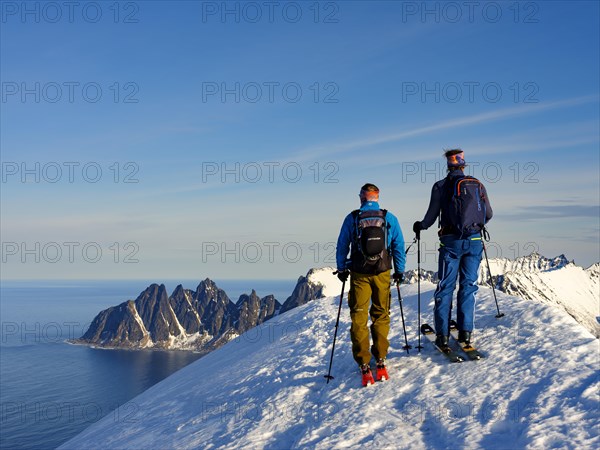 Two ski mountaineers at the summit of Husafjellet with a view over Devils Teeth
