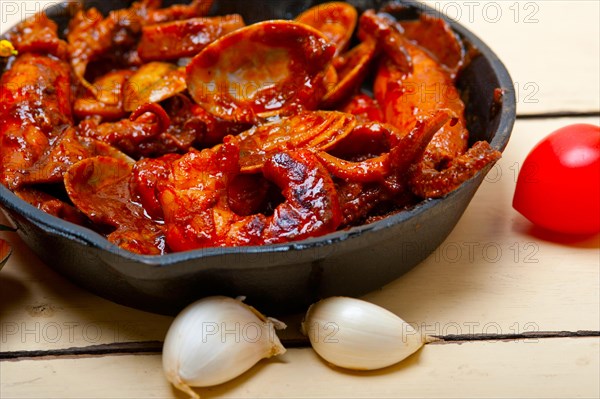 Fresh seafood stew prepared on an iron skillet ove white rustic wood table