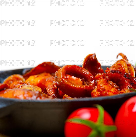 Fresh seafood stew prepared on an iron skillet ove white rustic wood table