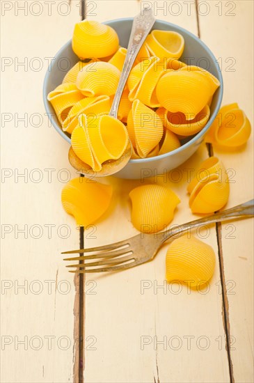 Raw Italian snail lumaconi pasta on a blue bowl over rustic table macro