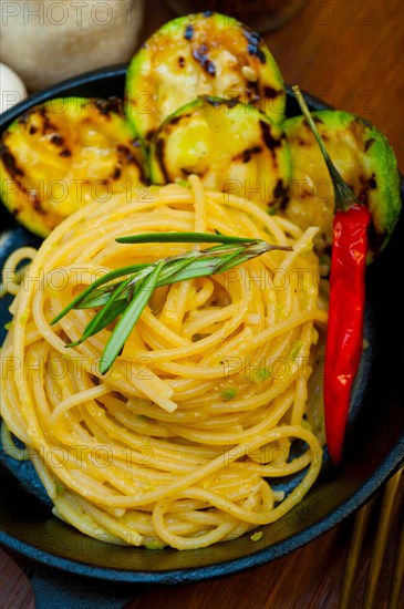 Italian spaghetti pasta with zucchini sauce on iron skillet over wood board