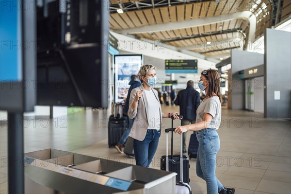 Two travelling women wearing protective masks discussing by flight information board at the Faro airport