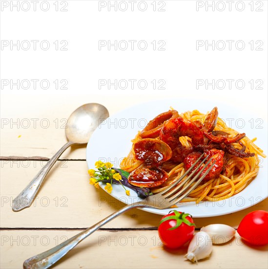 Italian seafood spaghetti pasta on red tomato sauce over white rustic wood table