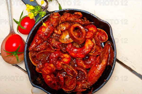 Fresh seafood stew prepared on an iron skillet ove white rustic wood table