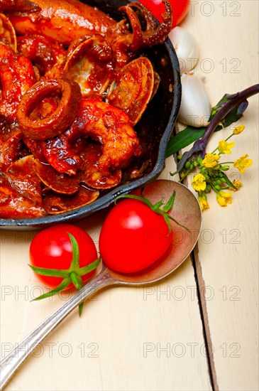 Fresh seafood stew prepared on an iron skillet ove white rustic wood table