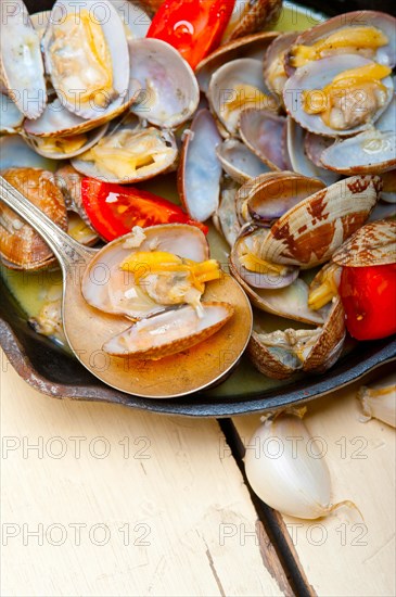 Fresh clams stewed on an iron skillet over wite rustic wood table