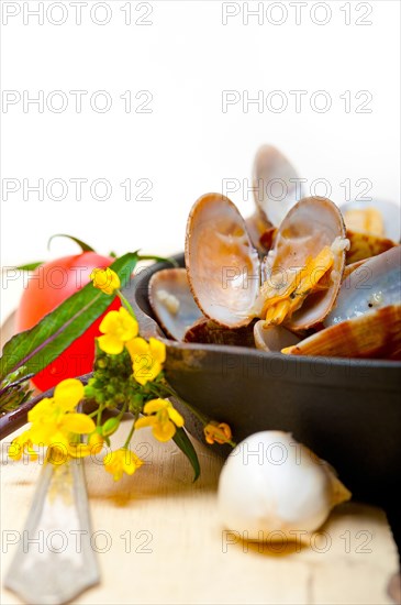 Fresh clams stewed on an iron skillet over wite rustic wood table