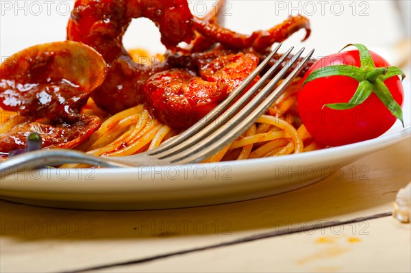 Italian seafood spaghetti pasta on red tomato sauce over white rustic wood table