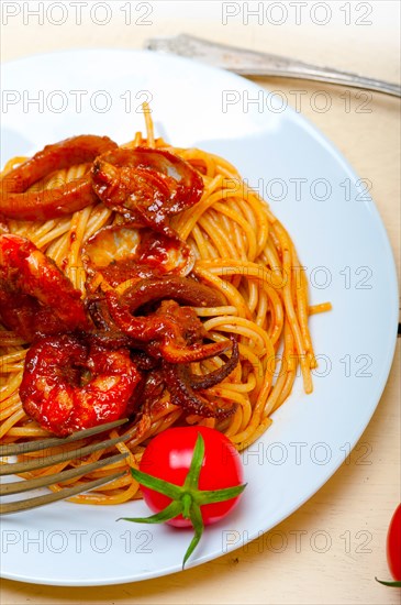 Italian seafood spaghetti pasta on red tomato sauce over white rustic wood table