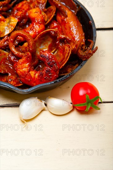 Fresh seafood stew prepared on an iron skillet ove white rustic wood table