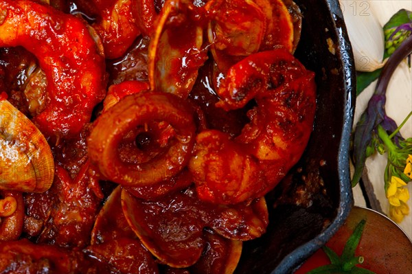 Fresh seafood stew prepared on an iron skillet ove white rustic wood table