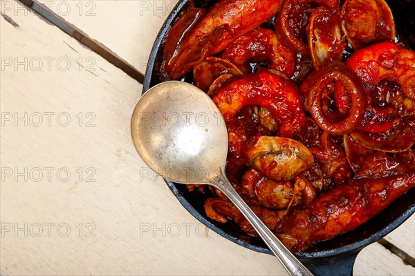 Fresh seafood stew prepared on an iron skillet ove white rustic wood table