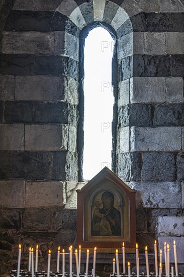 Burning candles in front of an image of the Virgin Mary in front of an open window of the church of San Pietro