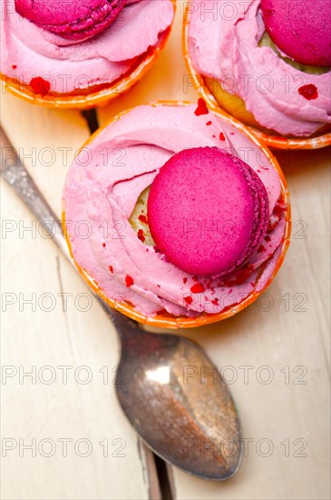 Fresh pink berry cream cupcake with macaroon on top over rustic wood table