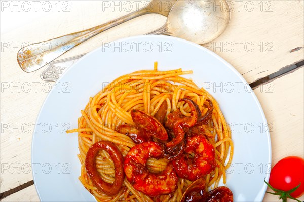 Italian seafood spaghetti pasta on red tomato sauce over white rustic wood table