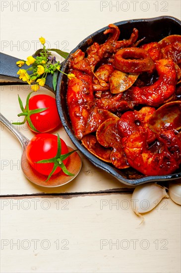 Fresh seafood stew prepared on an iron skillet ove white rustic wood table