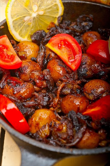 Baby cuttle fish roasted on iron skillet with tomatoes and onions over rustic wood table