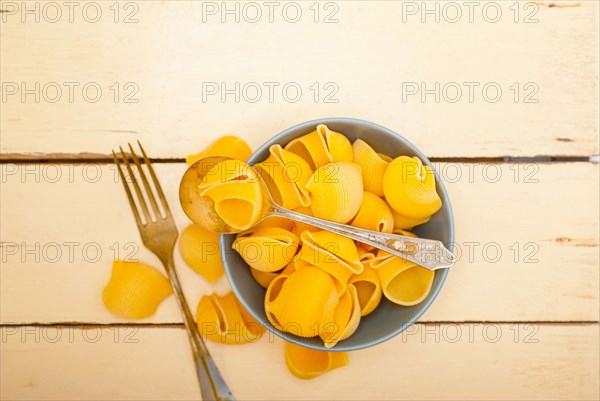 Raw Italian snail lumaconi pasta on a blue bowl over rustic table macro