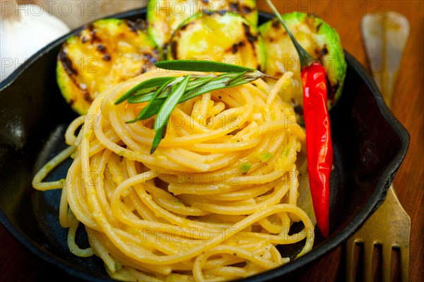 Italian spaghetti pasta with zucchini sauce on iron skillet over wood board