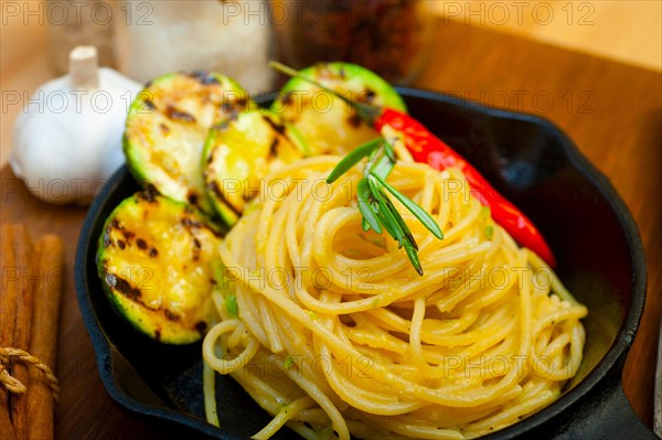 Italian spaghetti pasta with zucchini sauce on iron skillet over wood board