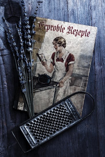 Old cookbook with lavender and kitchen grater on rustic background