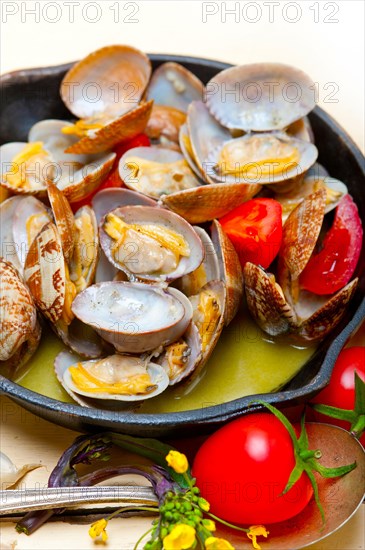 Fresh clams stewed on an iron skillet over wite rustic wood table