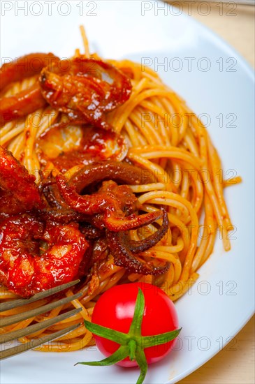 Italian seafood spaghetti pasta on red tomato sauce over white rustic wood table