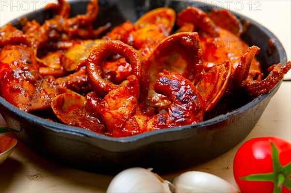 Fresh seafood stew prepared on an iron skillet ove white rustic wood table