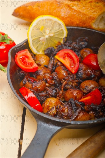 Baby cuttle fish roasted on iron skillet with tomatoes and onions over rustic wood table