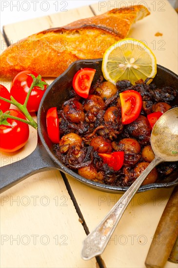 Baby cuttle fish roasted on iron skillet with tomatoes and onions over rustic wood table