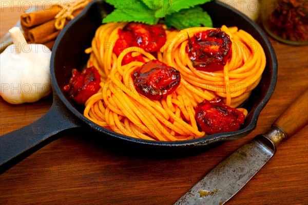 Italian spaghetti pasta and tomato with mint leaves on iron skillet over wood board