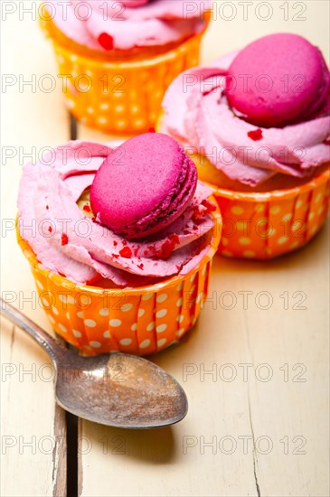 Fresh pink berry cream cupcake with macaroon on top over rustic wood table