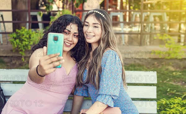 Two pretty girls sitting on a bench taking a selfie