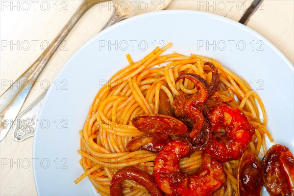 Italian seafood spaghetti pasta on red tomato sauce over white rustic wood table