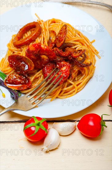 Italian seafood spaghetti pasta on red tomato sauce over white rustic wood table