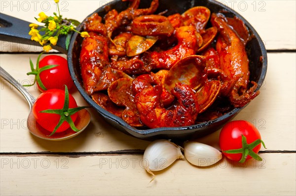 Fresh seafood stew prepared on an iron skillet ove white rustic wood table