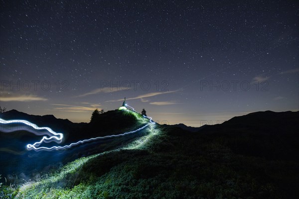 Green tent and tracer with headlamp under a starry sky on the Portlakopf