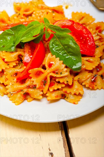 Italian pasta farfalle butterfly bow-tie with tomato basil sauce over white rustic wood table