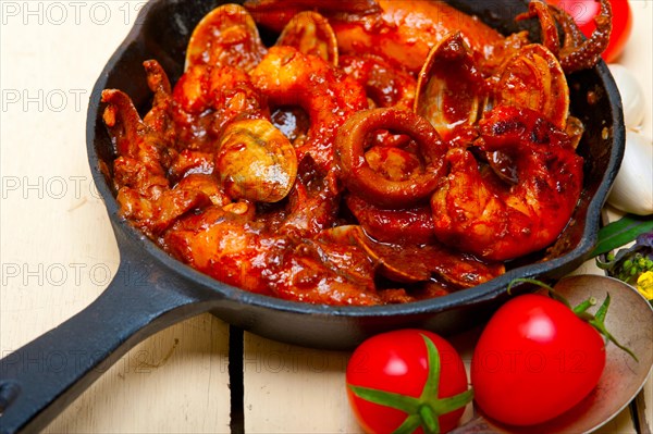 Fresh seafood stew prepared on an iron skillet ove white rustic wood table