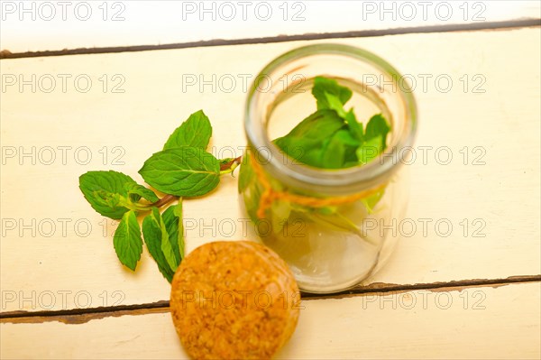 Fresh mint leaves on a glass jarover a rustic white wood table