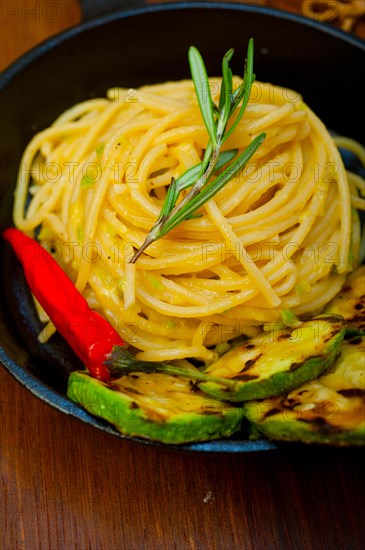 Italian spaghetti pasta with zucchini sauce on iron skillet over wood board